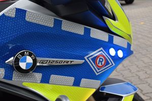 Owiewka boczna motocykla oklejona odblaskowa folią koloru  niebieskiego  z żółtymi wstawkami oraz znak ruchu drogowego i oznaczenie marki i modelu motocykla. BMW  R 1250 RT.