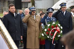 Delegacja służb mundurowych na cmentarzu komunalnym pod pomnikiem Lotników Polskich. Umundurowany policjant, strażak i żołnierz oddają honory salutując.