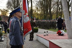 Poczet sztandarowy oleskich policjantów stoi pod pomnikiem Lotników Polskich. W tle szpaler żołnierzy.