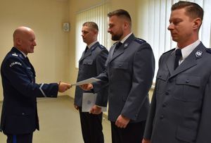 Trzech policjantów stoi w szeregu, Komendant Powiatowy Policji insp. Tomasz Kubicki podaje rękę  policjantowi stojącemu w środku.