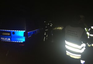 Policyjny radiowóz i policjanci na miejscu poszukiwań zaginionego grzybiarza. W całkowitej ciemności widoczne kamizelki i elementy odblaskowe oraz napis POLICJA na radiowozie,