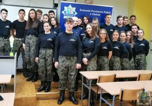 Uczniowie klasy mundurowej pozują do zdjęcia grypowego. W tle widoczny niebieski baner z napisem Komenda Powiatowa Policji w Oleśnie oraz logiem Policji.